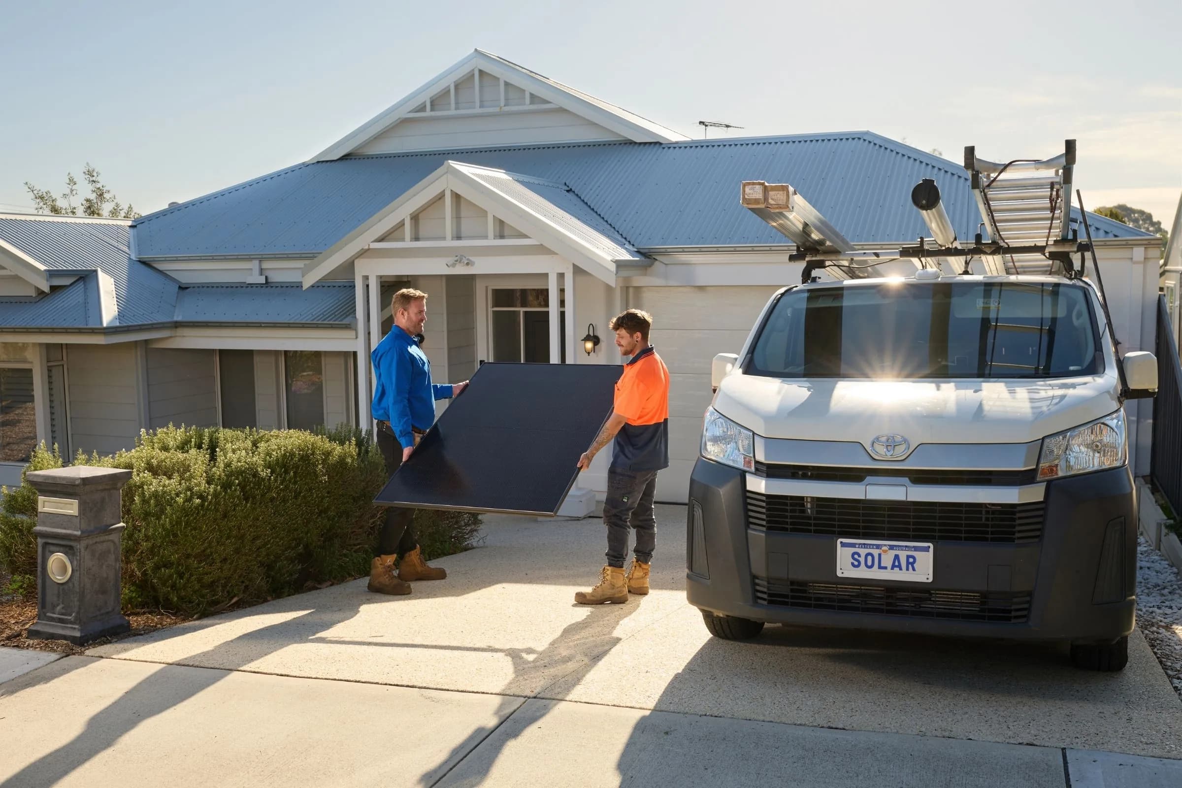 Installers carrying a solar panel outside a Perth home