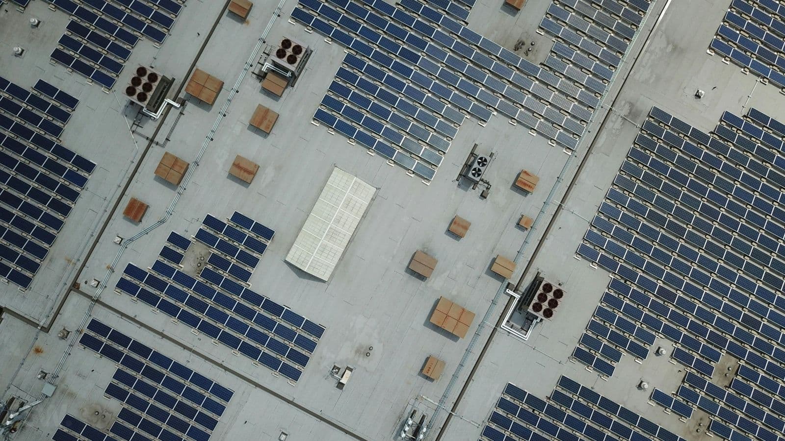 Aerial view of solar panel arrays across a large commercial roof, with rooftop ventilation and air-conditioning equipment.
