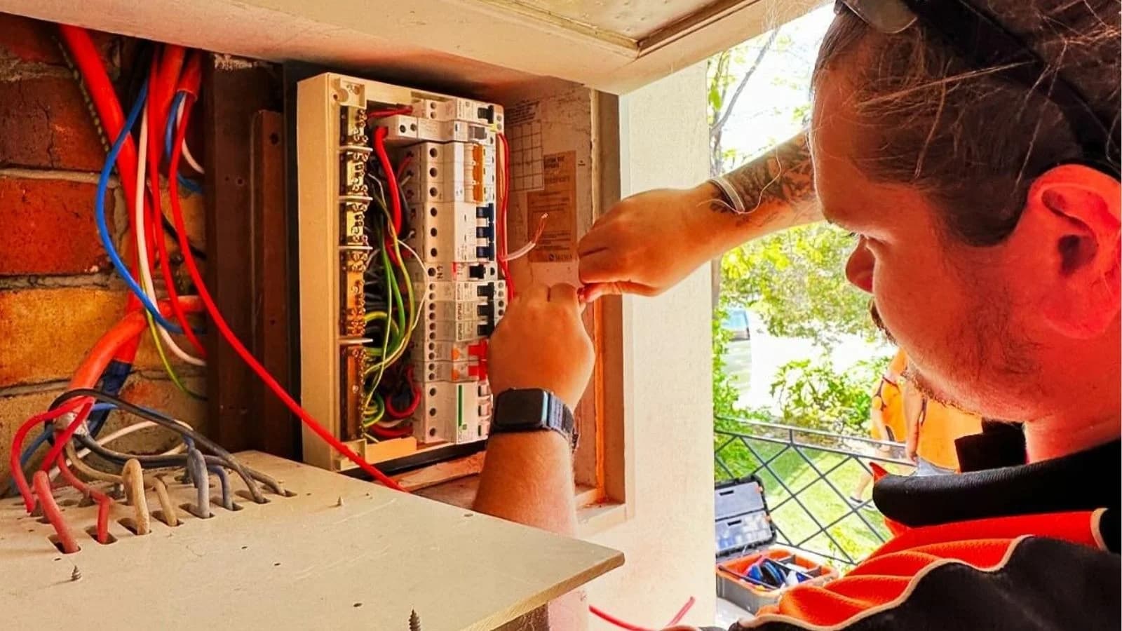 Electrician working on wiring inside an open residential switchboard.