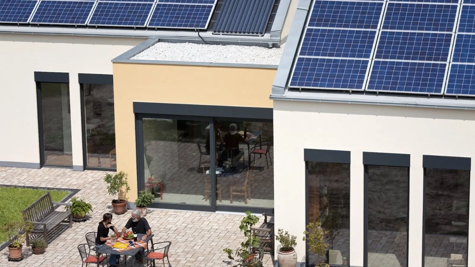 Rooftop solar panels on a home with two people seated at a patio table.