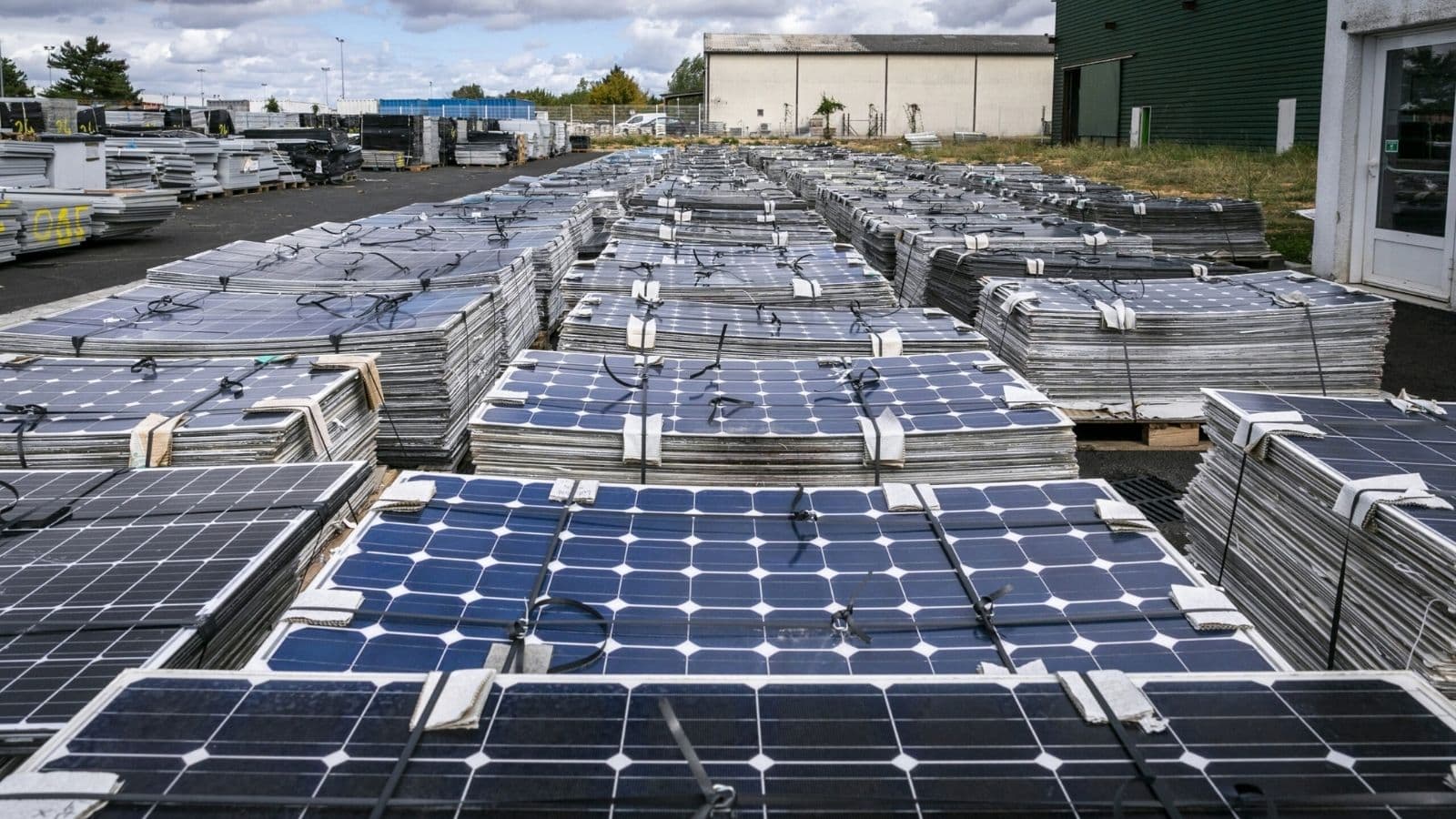 Rows of used solar panels stacked on pallets in an outdoor industrial yard.