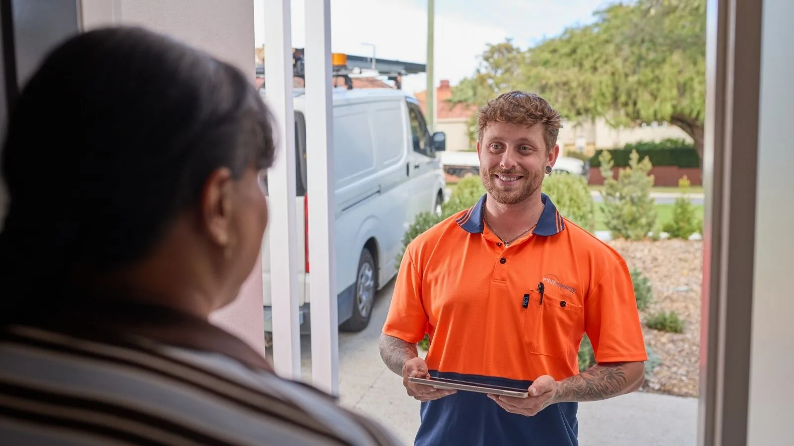 A PSW Energy consultant with a tablet at a Perth customer's front door, branded van behind him